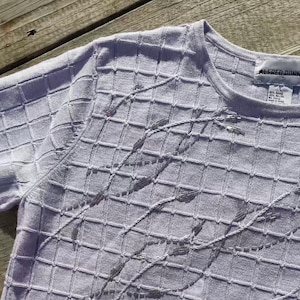 May include: A white sweater with a grid pattern and beaded embellishments. The sweater has a crew neck and long sleeves. The label reads "Alfred Dunner".