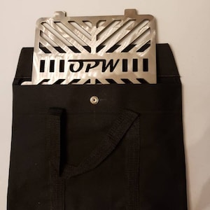 May include: A black canvas bag with two handles and a metal grill with the text "OPWIII" inside. The bag has a button closure.