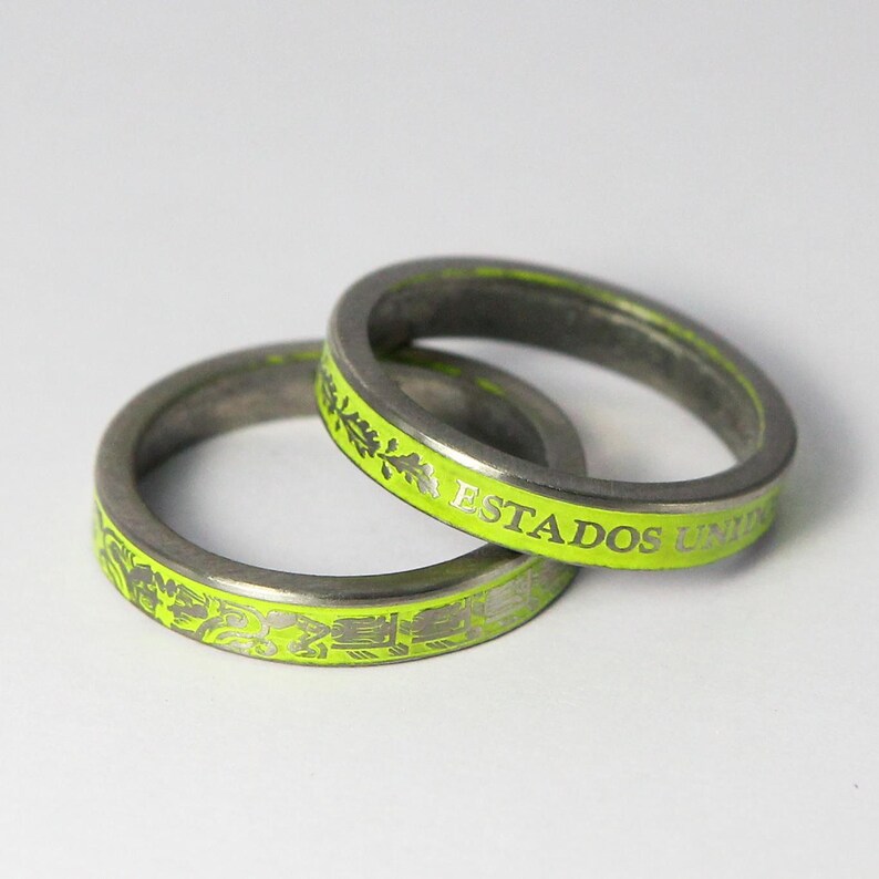 K&ouml;nnte beinhalten: Zwei silberne Ringe mit einer leuchtend gr&uuml;nen Emaille-Oberfl&auml;che. Die Ringe sind mit den Worten "Estados Unidos" und einem floralen Design graviert.