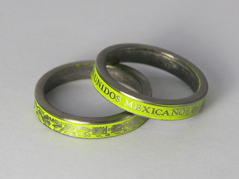 K&ouml;nnte beinhalten: Zwei silberne Ringe mit einer leuchtend gelben Inschrift. Die Inschrift auf einem Ring lautet "UNIDOS MEXICANOS". Der andere Ring hat ein dekoratives Design.