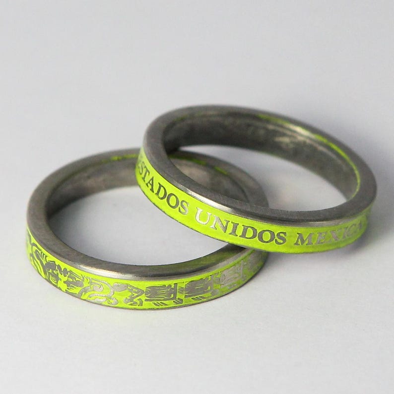 K&ouml;nnte beinhalten: Zwei silberne Ringe mit einem leuchtend gelben Emailleband. Der obere Ring tr&auml;gt die Worte "Estados Unidos Mexico" auf dem Band eingraviert. Der untere Ring hat ein dekoratives Muster.