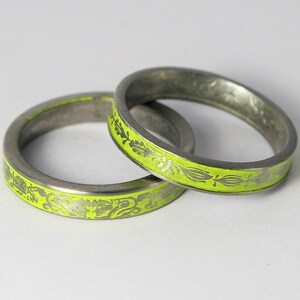 K&ouml;nnte beinhalten: Zwei silberne Ringe mit einem Band aus lindgr&uuml;nem Emaille und einem silbernen Blumendesign.