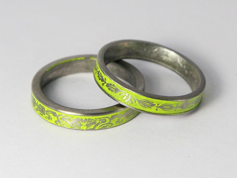 K&ouml;nnte beinhalten: Zwei silberne Ringe mit einem Band aus lindgr&uuml;nem Emaille und einem silbernen Blumendesign.