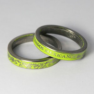 K&ouml;nnte beinhalten: Zwei silberne Ringe mit einem leuchtend gr&uuml;nen Emailleband. Der obere Ring tr&auml;gt die Worte "UNIDOS MEXICANOS" auf dem Band eingraviert. Der untere Ring hat ein dekoratives Design.