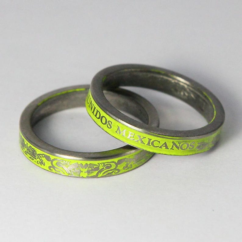 K&ouml;nnte beinhalten: Zwei silberne Ringe mit einem leuchtend gr&uuml;nen Emailleband. Der obere Ring tr&auml;gt die Worte "UNIDOS MEXICANOS" auf dem Band eingraviert. Der untere Ring hat ein dekoratives Design.