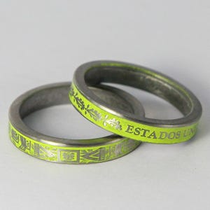 K&ouml;nnte beinhalten: Zwei silberne Ringe mit einer leuchtend gelben Emaille-Oberfl&auml;che. Ein Ring tr&auml;gt die Worte "ESTADOS UNIDOS" auf der Band. Der andere Ring hat ein dekoratives Muster.