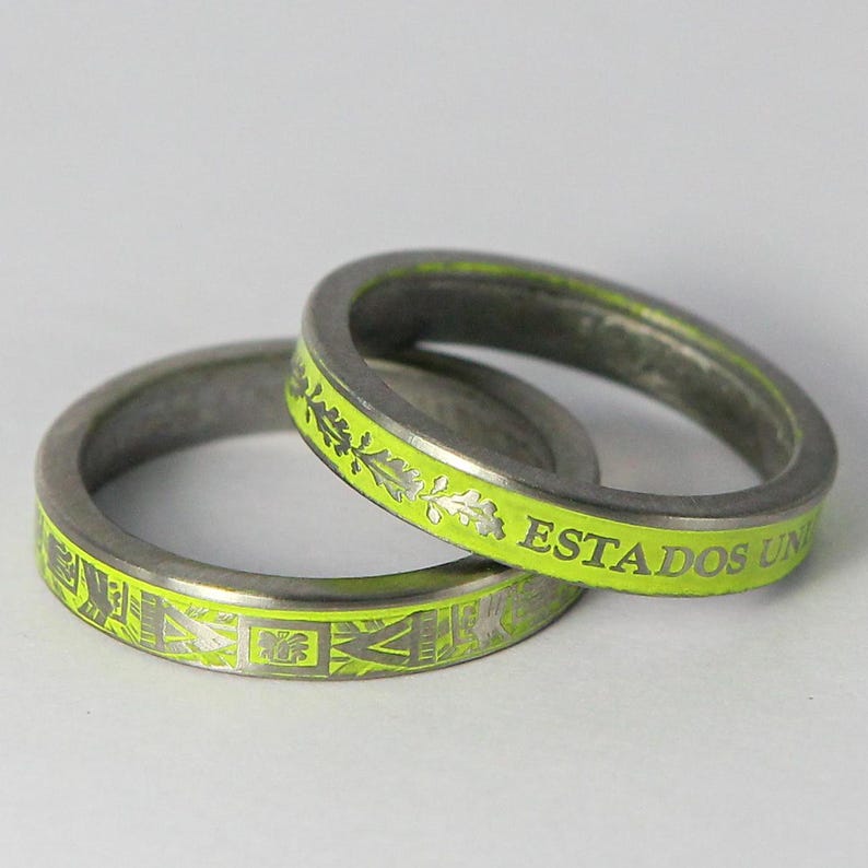 K&ouml;nnte beinhalten: Zwei silberne Ringe mit einer leuchtend gelben Emaille-Oberfl&auml;che. Ein Ring tr&auml;gt die Worte "ESTADOS UNIDOS" auf der Band. Der andere Ring hat ein dekoratives Muster.