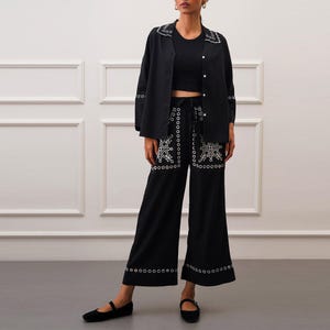 May include: Black embroidered pants with a wide leg and a black shirt with white embroidery around the collar and cuffs.