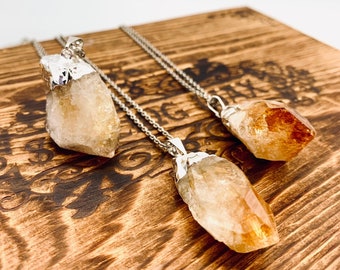 May include: Three raw citrine crystal pendants on silver chains. The crystals are different sizes and shapes, with a light yellow to orange color.