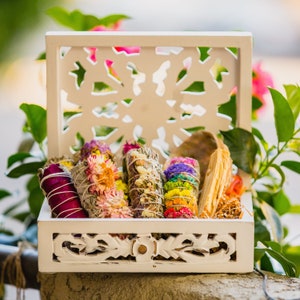 May include: A white wooden box with intricate carvings holds a collection of colourful dried flower bundles. The bundles are made with dried herbs and flowers, and they are arranged in a decorative pattern.