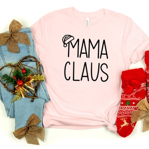 May include: A pink t-shirt with the text "Mama Claus" in black lettering. The shirt is paired with a pair of red and white patterned socks with pom-poms.
