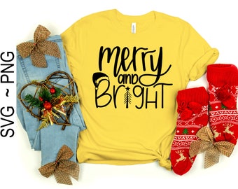 May include: A yellow t-shirt with the text "merry and bright" in black lettering. The shirt is decorated with a small Christmas tree and a Santa hat. The shirt is laid out on a white surface with a pair of red and white patterned socks and a brown bow.