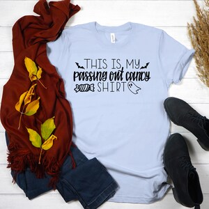 May include: A light blue t-shirt with the text "This is my passing out candy shirt" in black. The shirt is decorated with a ghost and candy corn graphic.