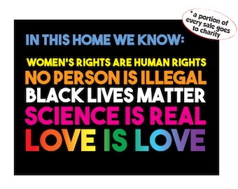 May include: A black and white poster with the text "IN THIS HOME WE KNOW:" followed by a list of statements in different colours: "WOMEN'S RIGHTS ARE HUMAN RIGHTS", "NO PERSON IS ILLEGAL", "BLACK LIVES MATTER", "SCIENCE IS REAL", and "LOVE IS LOVE". A small sticker in the top right corner says "*a portion of every sale goes to charity".