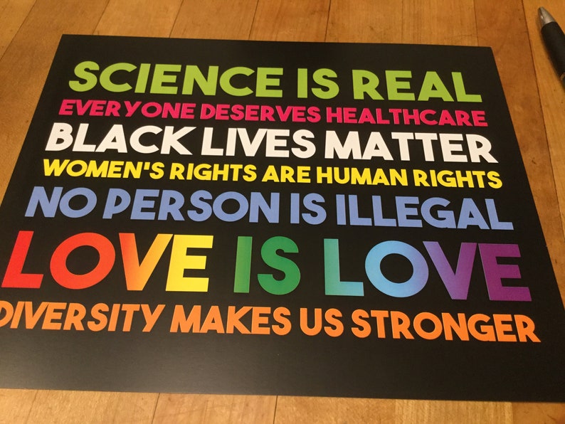 May include: A black and white poster with the text "SCIENCE IS REAL", "EVERYONE DESERVES HEALTHCARE", "BLACK LIVES MATTER", "WOMEN'S RIGHTS ARE HUMAN RIGHTS", "NO PERSON IS ILLEGAL", "LOVE IS LOVE", and "DIVERSITY MAKES US STRONGER".