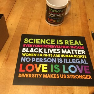 May include: A black and white poster with the text "SCIENCE IS REAL", "EVERYONE DESERVES HEALTHCARE", "BLACK LIVES MATTER", "WOMEN'S RIGHTS ARE HUMAN RIGHTS", "NO PERSON IS ILLEGAL", "LOVE IS LOVE", and "DIVERSITY MAKES US STRONGER" in different colours.