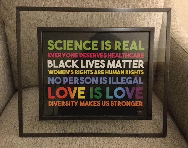 May include: Framed print with a black background and white text that reads "Science is real", "Everyone deserves healthcare", "Black lives matter", "Women's rights are human rights", "No person is illegal", "Love is love", and "Diversity makes us stronger".