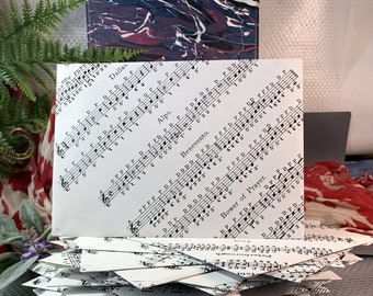 May include: A stack of white envelopes with musical notes printed on them. The envelopes are folded in half and stacked on top of each other. The top envelope has the words "Dallas", "Alps", "Benevento", and "Bower of Prayer" printed on it.