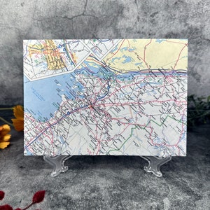 May include: A vintage map of the northeastern United States, showing the state of New York and surrounding areas. The map is printed on paper and has a light blue, yellow, and green color scheme. The map is displayed on a clear plastic stand.