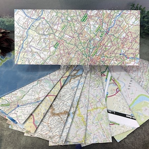 May include: A collection of vintage paper maps, some folded and some flat, with various locations and scales. The maps are in shades of blue, green, brown, and white, with black lines and text.