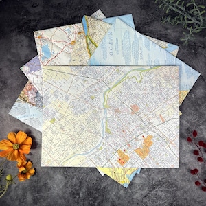May include: A collection of folded map paper, showcasing various geographical regions. The maps feature detailed road networks, city layouts, and geographical features. The color palette includes shades of beige, blue, and yellow, with a dark background.