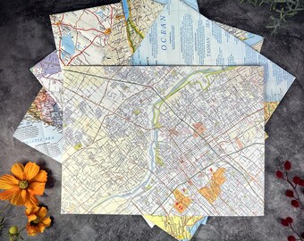 May include: A collection of folded map paper, showcasing various geographical regions. The maps feature detailed road networks, city layouts, and geographical features. The color palette includes shades of beige, blue, and yellow, with a dark background.