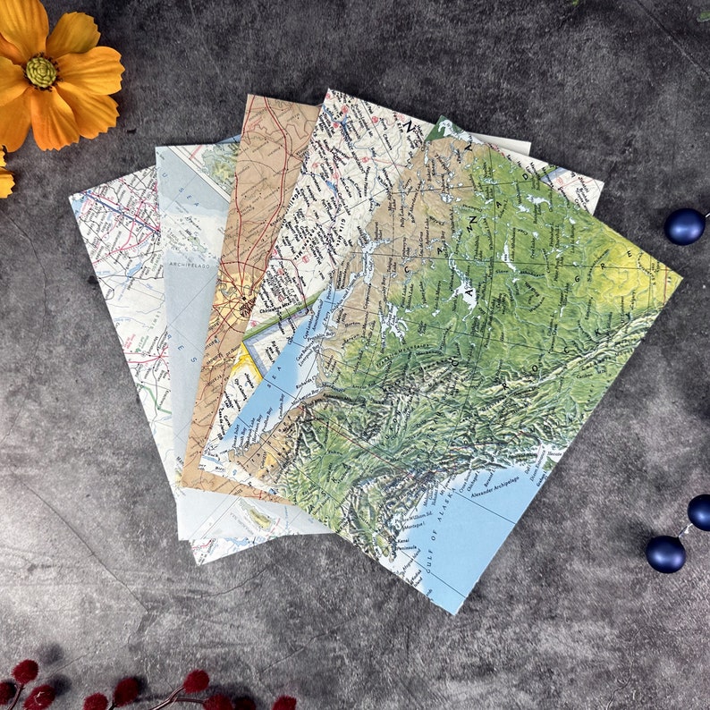 May include: A stack of vintage maps with a green, blue, and brown color scheme. The maps are folded and show different geographical areas. The maps are on a gray background.