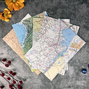 May include: A stack of vintage paper maps with different locations, including a map of the Gulf of Alaska and a map of New England. The maps are in various shades of blue, green, and brown.