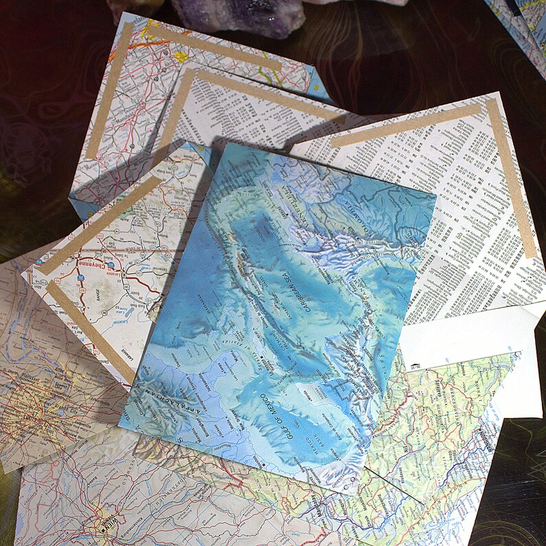 May include: A collection of vintage maps, some folded and some unfolded, with a blue map of the Gulf of Mexico and Caribbean Sea on top. The maps are on a brown surface.