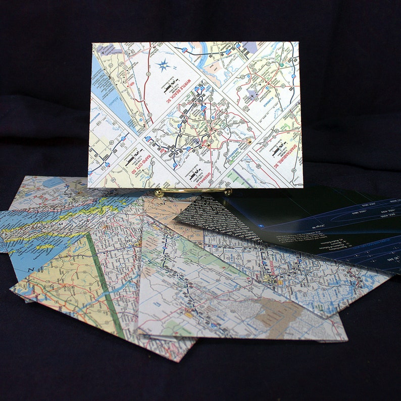 May include: A collection of folded maps, some with road maps and some with city maps, are stacked on top of each other. The maps are all different sizes and colors. The maps are on a black surface.