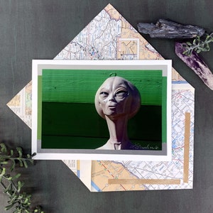 May include: A close-up of a gray alien sculpture with a green background. The sculpture has large eyes and a small mouth. The sculpture is made of a smooth material and has a realistic appearance.