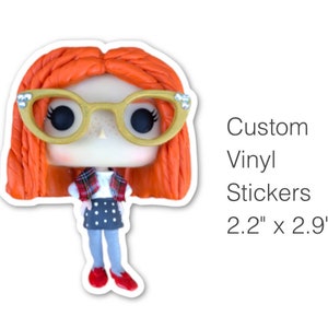 Peut inclure: Un autocollant en vinyle personnalisé représentant une fille de dessin animé aux cheveux roux, portant des lunettes, une chemise à carreaux, une jupe à pois et des chaussures rouges. L'autocollant mesure 2,2 pouces par 2,9 pouces.