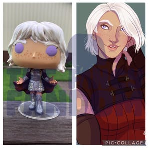 May include: A custom-made pop figure of a woman with white hair, wearing a silver and red outfit. The figure is standing on a clear plastic base. The figure is next to a digital illustration of the same woman.