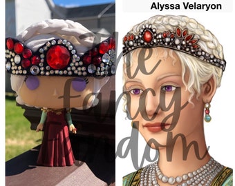 Può includere: Una figura pop personalizzata di una regina che indossa una corona nera e argentata con gemme rosse. La corona è decorata con strass e la figura indossa un abito rosso. Il testo "Queen Alyssa Velaryon" è visibile sullo sfondo.