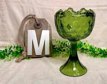 May include: A green glass pedestal bowl with a diamond pattern. The bowl has a scalloped edge and a wide base.