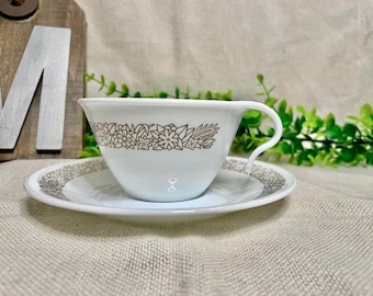 May include: White teacup and saucer with a gold floral pattern. The cup has a handle and the saucer has a scalloped edge.