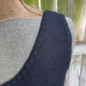 May include: Close-up of the neckline of a black sleeveless top with a decorative stitch detail.