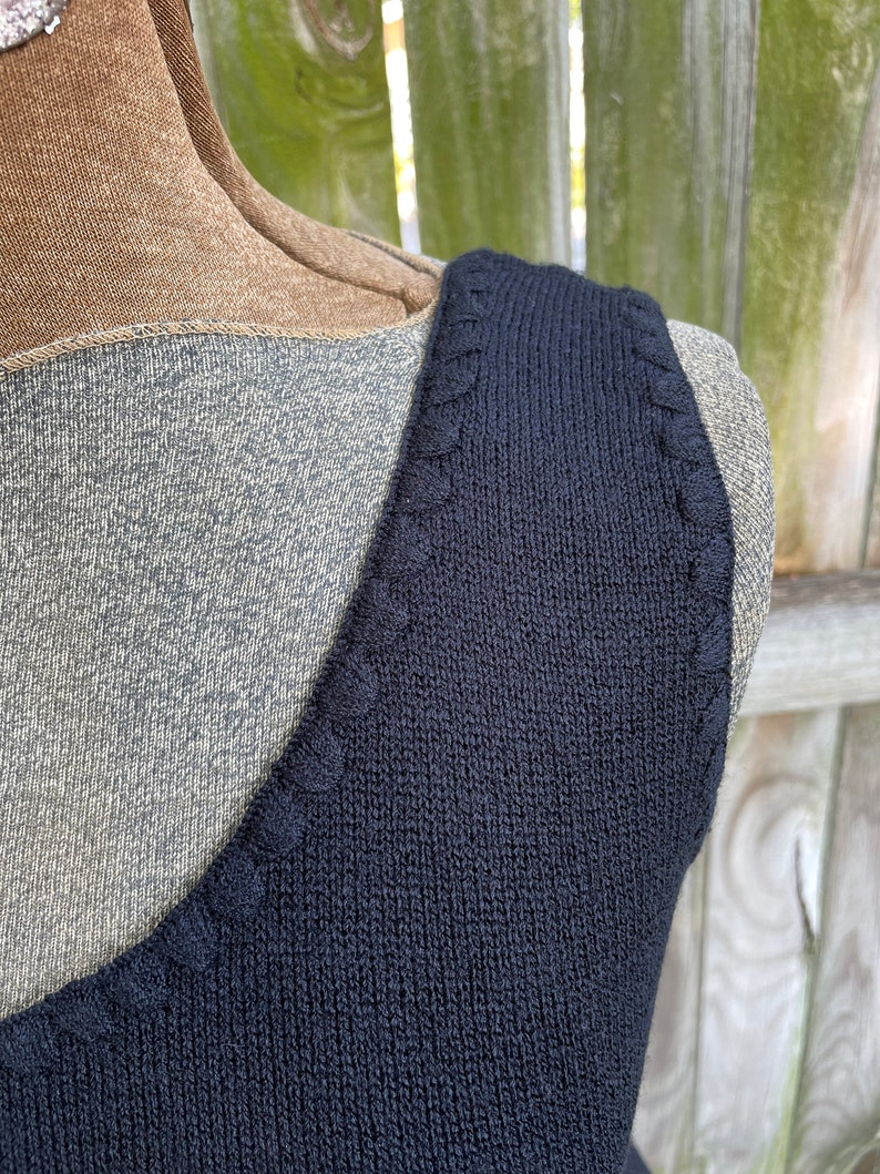 May include: Close-up of the neckline of a black sleeveless top with a decorative stitch detail.