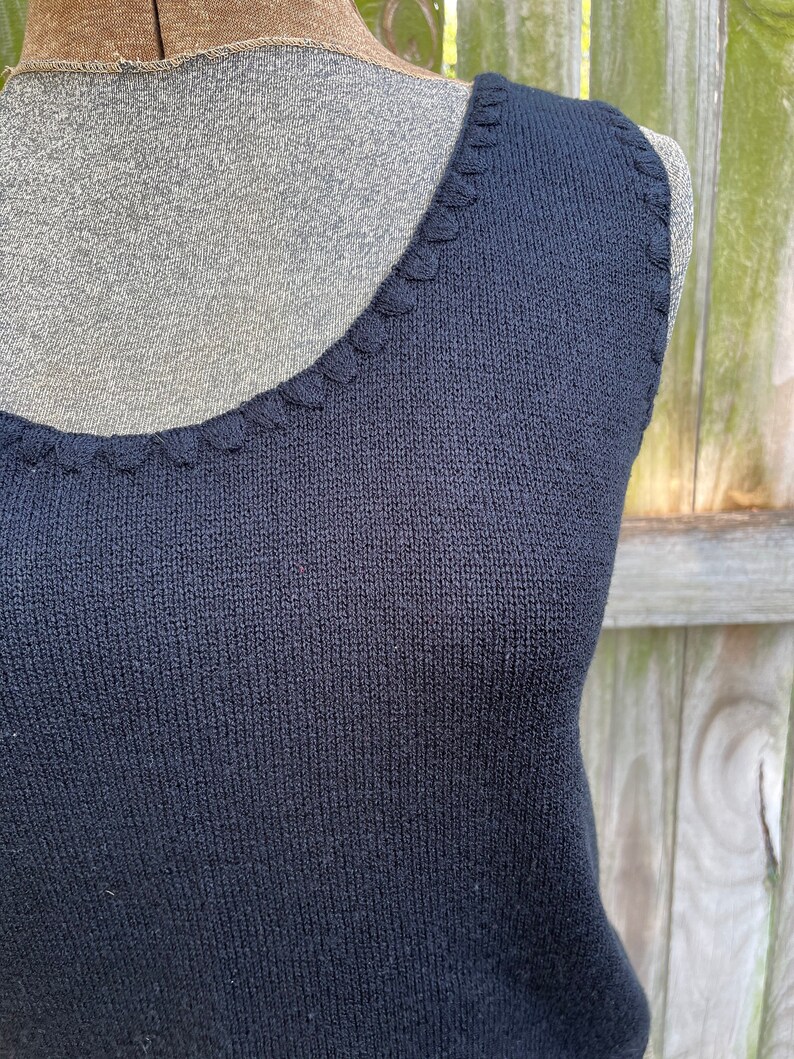 May include: A black sleeveless knitted top with a scalloped neckline.