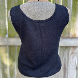 May include: A black sleeveless knitted top with a scalloped neckline.