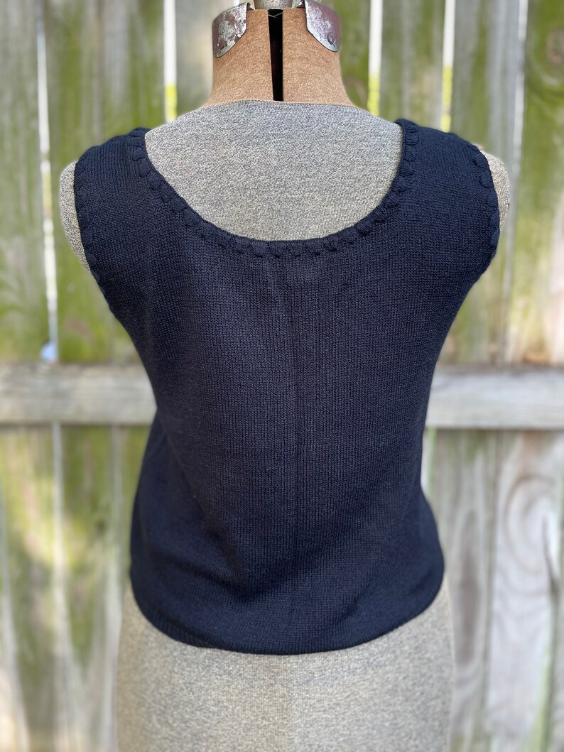May include: A black sleeveless knitted top with a scalloped neckline.