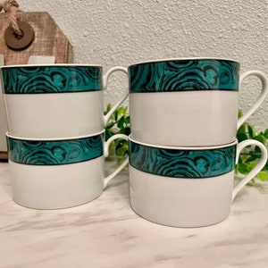 Könnte beinhalten: Set aus vier weißen Keramik-Kaffeetassen mit einem teal- und grün marmorierten Design. Die Tassen haben eine abgerundete Form und einen Henkel an der Seite.