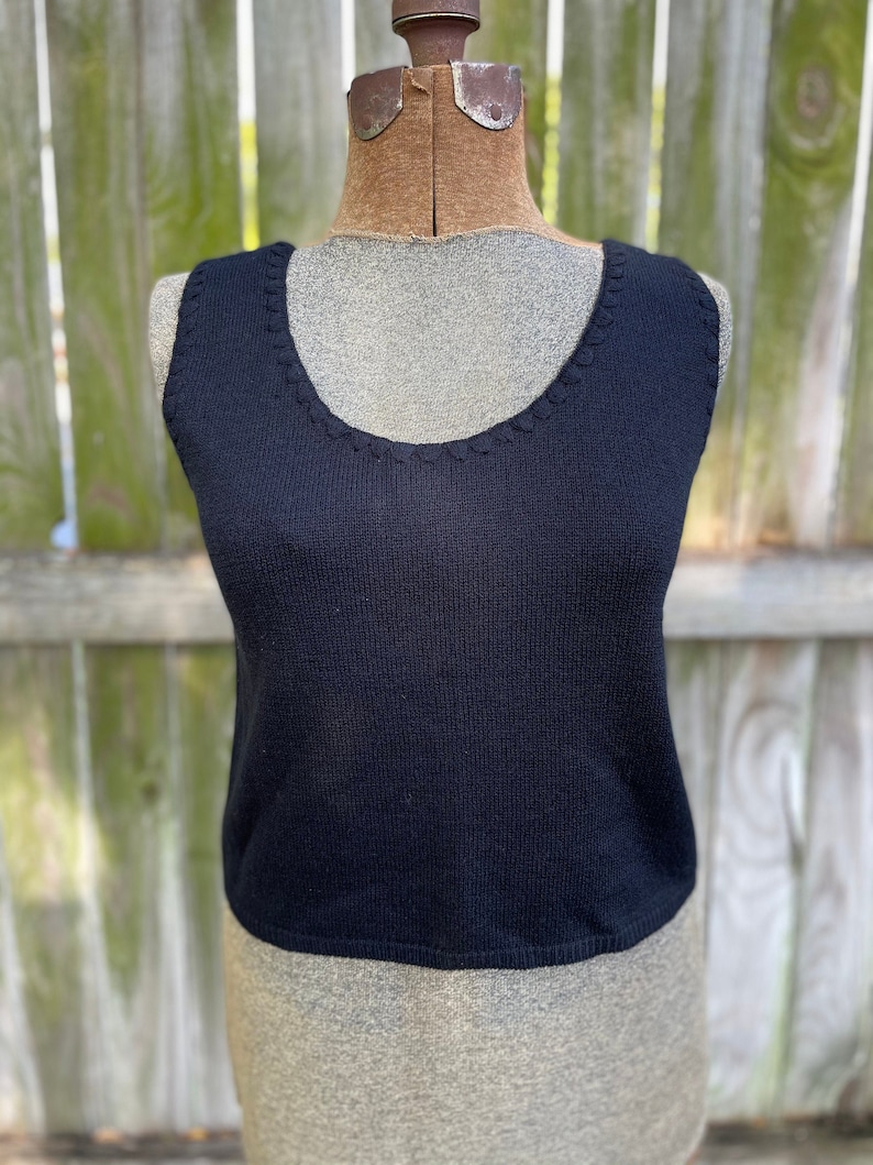 May include: A black sleeveless knitted top with a round neckline. The top is made of a fine knit fabric and has a slightly cropped length.