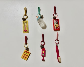 Dijes de plástico retro de los años 80: termómetro, biberón, ábaco, calculadora amarilla, señal de tráfico rosa y cepillo de dientes rosa.