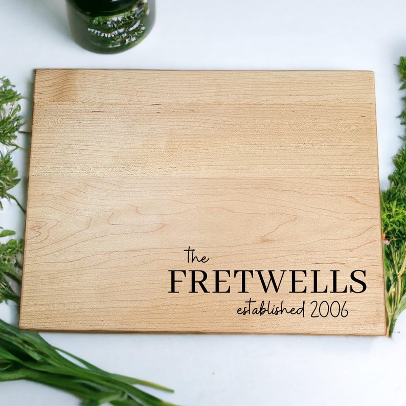 May include: A light brown wooden cutting board with the text "The Fretwells established 2006" engraved in black.