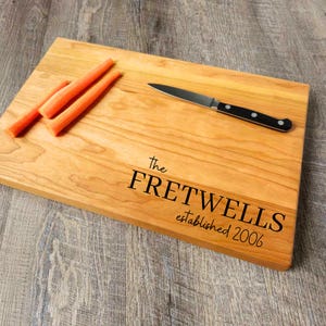 May include: A wooden cutting board with the text "The Fretwells established 2006" engraved on it. There are three orange carrots on the board and a small knife.