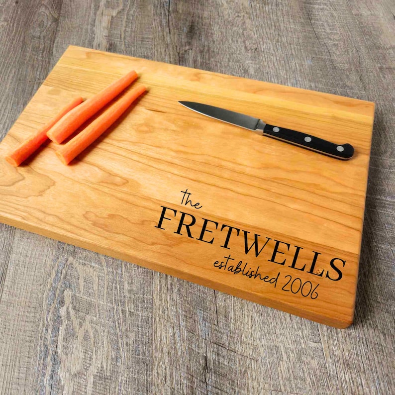 May include: A wooden cutting board with the text "The Fretwells established 2006" engraved on it. There are three orange carrots on the board and a small knife.