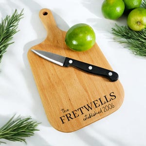 May include: A wooden cutting board with a handle, a small knife, and the text "The Fretwells established 2006".