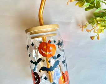 May include: A clear glass tumbler with a bamboo lid and a brown glass straw. The tumbler has a Halloween theme with black bats and orange pumpkins printed on the side.