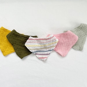 May include: Five cotton baby bibs in different colours and patterns. The bibs are in a triangular shape and have a textured surface. The colours are yellow, green, pink, and a striped pattern of pink, white, and grey.